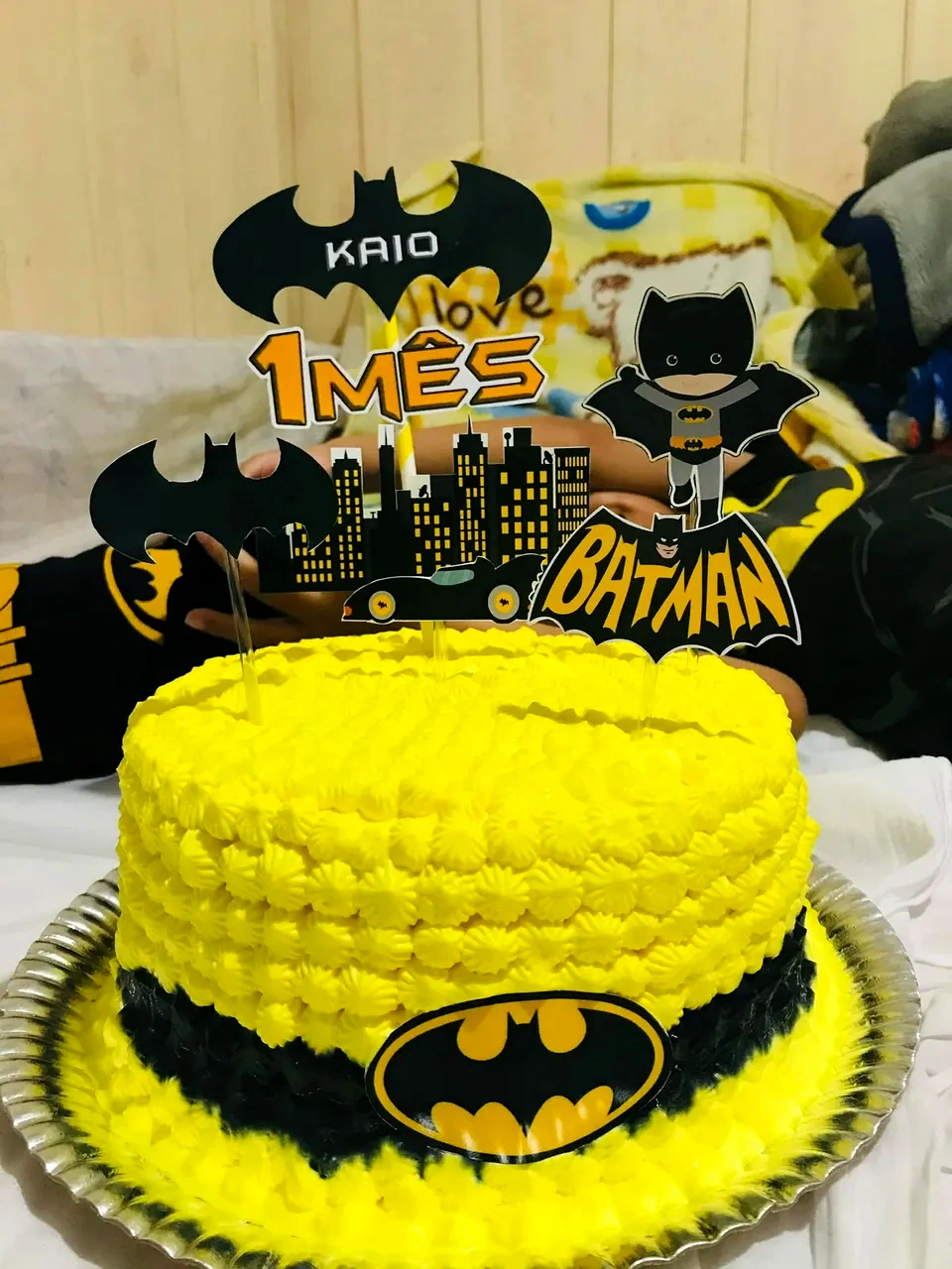 Bolo amarelo com faixa preta e símbolo do Batman, decorado com toppers do morcego, da cidade e do Batmóvel.