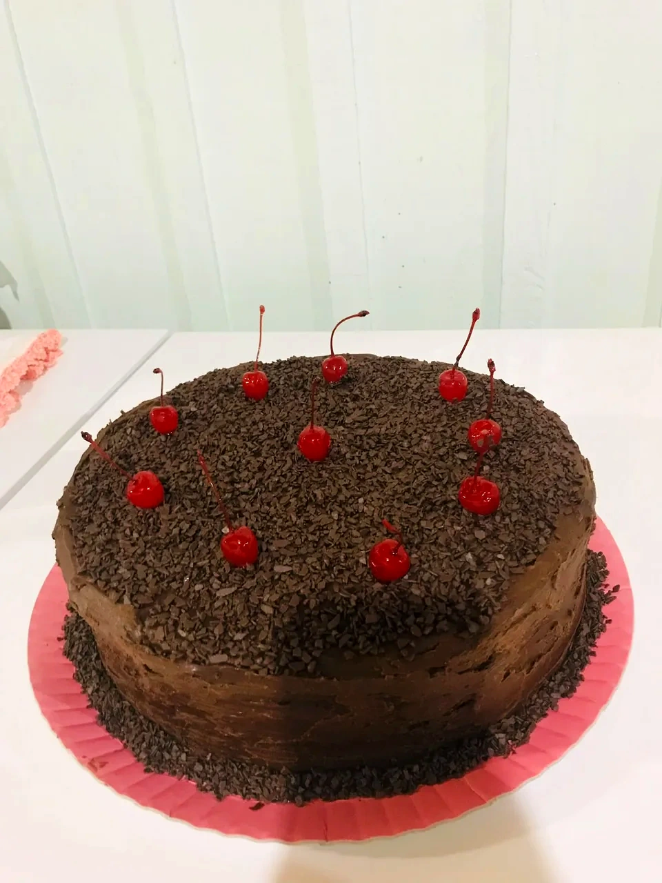 Bolo com cobertura de chocolate e raspas de chocolate, decorado com cerejas vermelhas no topo.