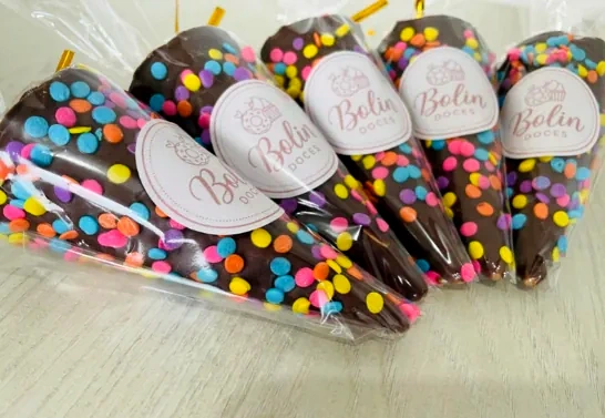 Cinco cones de chocolate com confeitos coloridos e etiqueta Bolin Doces, embalados em celofane com laço dourado.