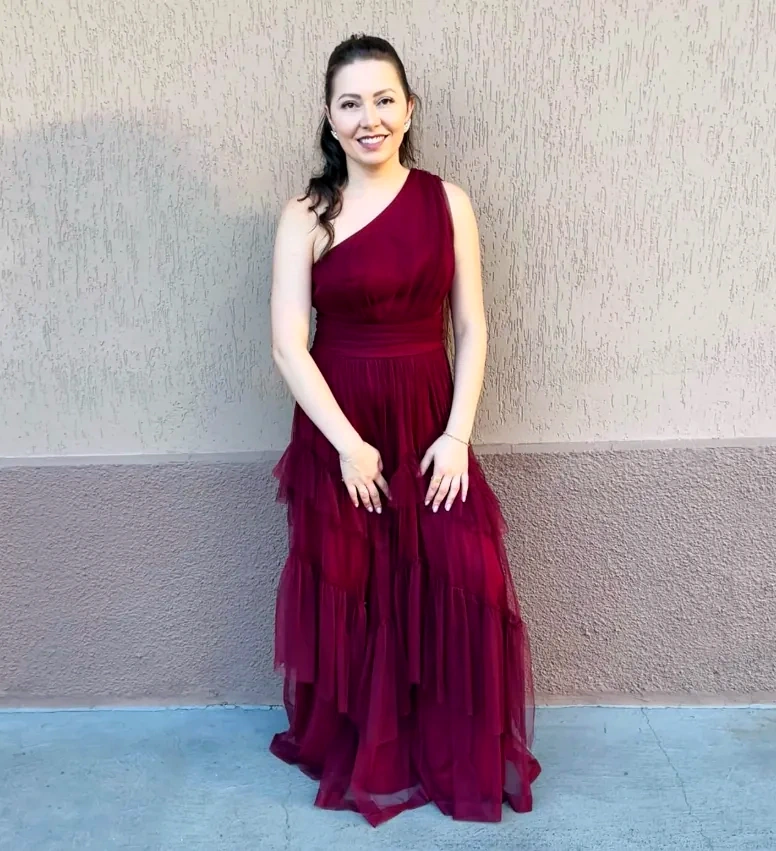 Patricia Bolin sorrindo, de vestido longo vinho, em frente a uma parede.